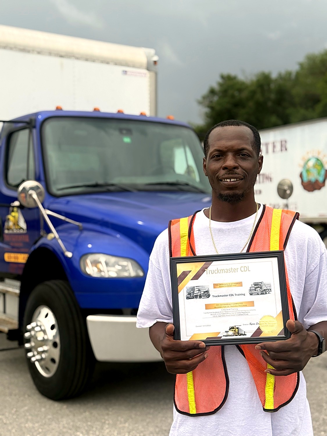 TruckMaster CDL graduate holding his completion certificate in front of a training truck